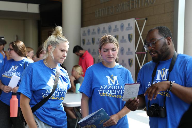 3名身穿圣母大学t恤的学生在迎新活动中，一边听着对方的演讲，一边专注地看着一张纸